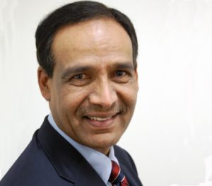Close-up of a smiling middle-aged Indian man in a blue suit and red and blue striped tie.