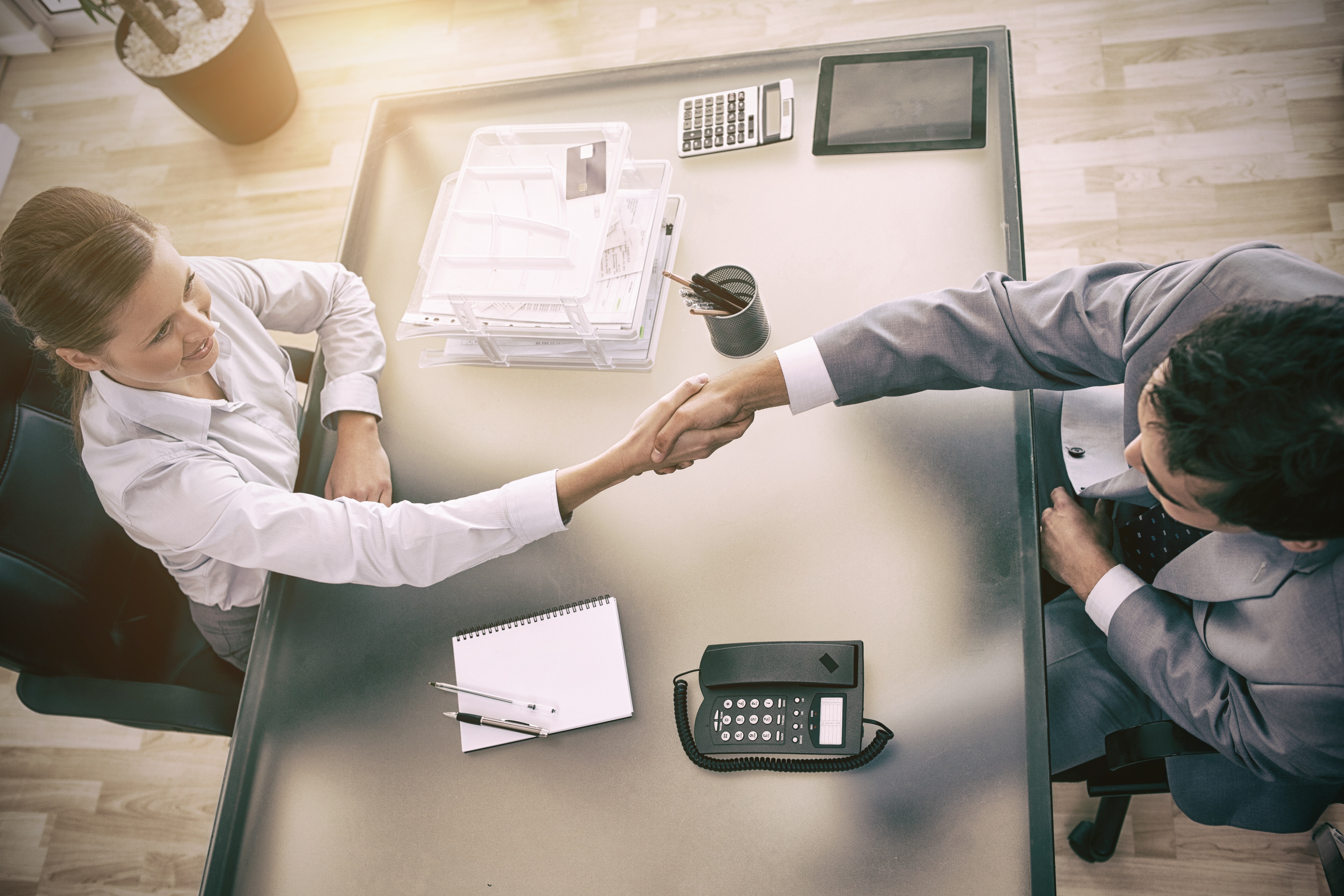 Aerial view of a modern business meeting between a man and a woman, shaking hands from two opposing sides of a desk.