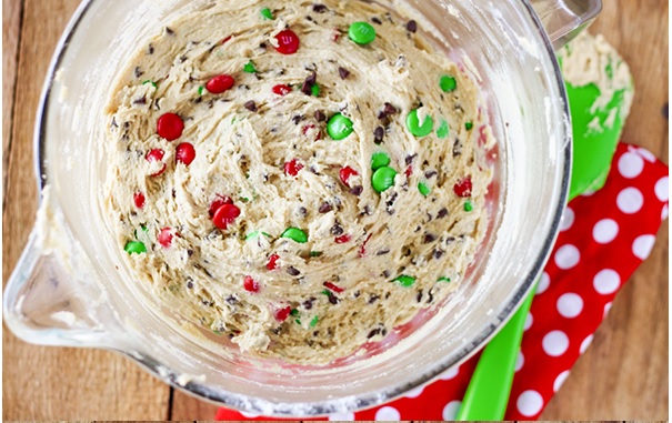 Baking bowl filled with cookie batter and M&M's, sitting on a wooden table on top of a red and white polka dotted napkin.