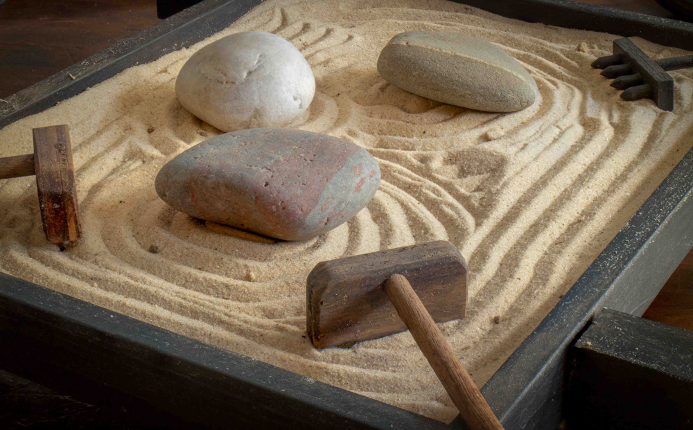 Rocks and rakes in a miniature sand garden with a maze-like design drawn into it.