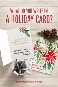 Floral Christmas cards on a table with pine cones, mug, and pens; the text above reads 'What do you write in a holiday card?' in red.