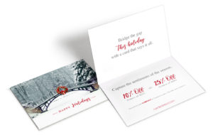 Exterior and interior shots of a holiday greeting card with a winter landscape on the front that includes a bridge with red wreath.