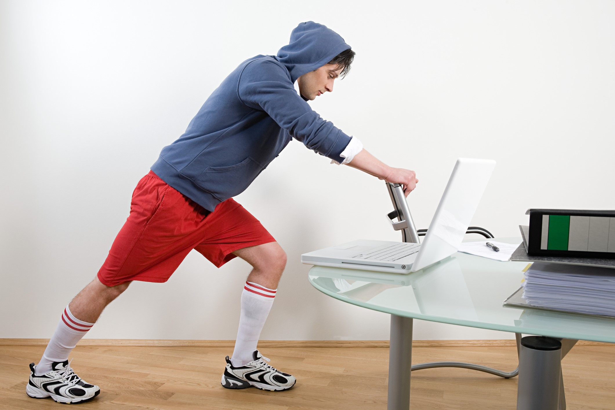 Man stretching with a chair at the office in  red gym shorts.