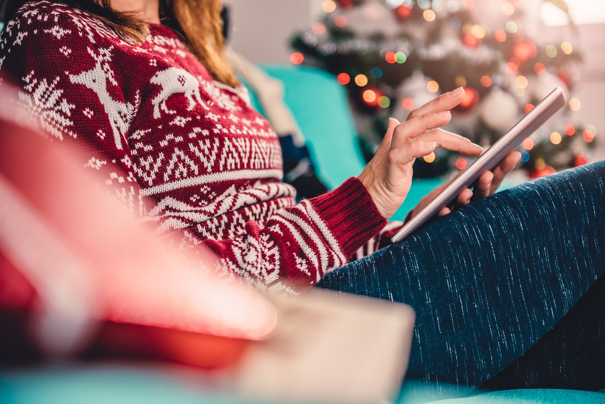 Women sitting on the blue sofa by the christmas tree and using tablet