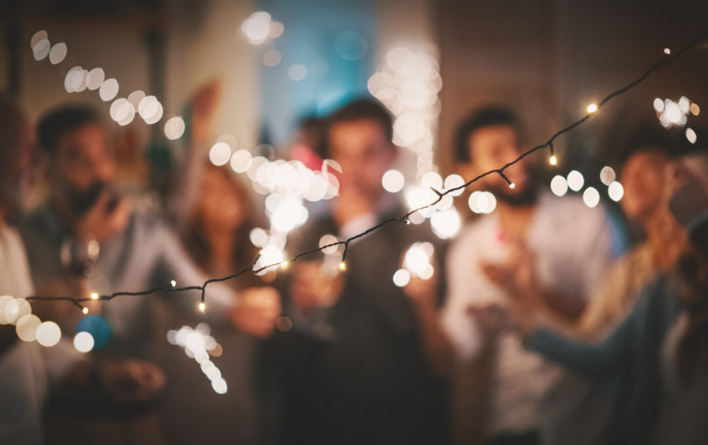 Closeup of group of  mixed age people having New year's party at home. They are having champagne, dancing and laughing. They are all out of focus and a string light in front of them is sharp