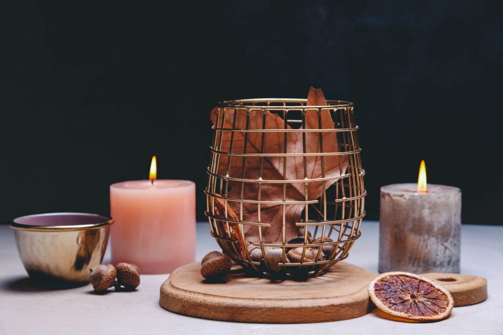 Beautiful burning candles and small cup of tea, autumn decor on black background.