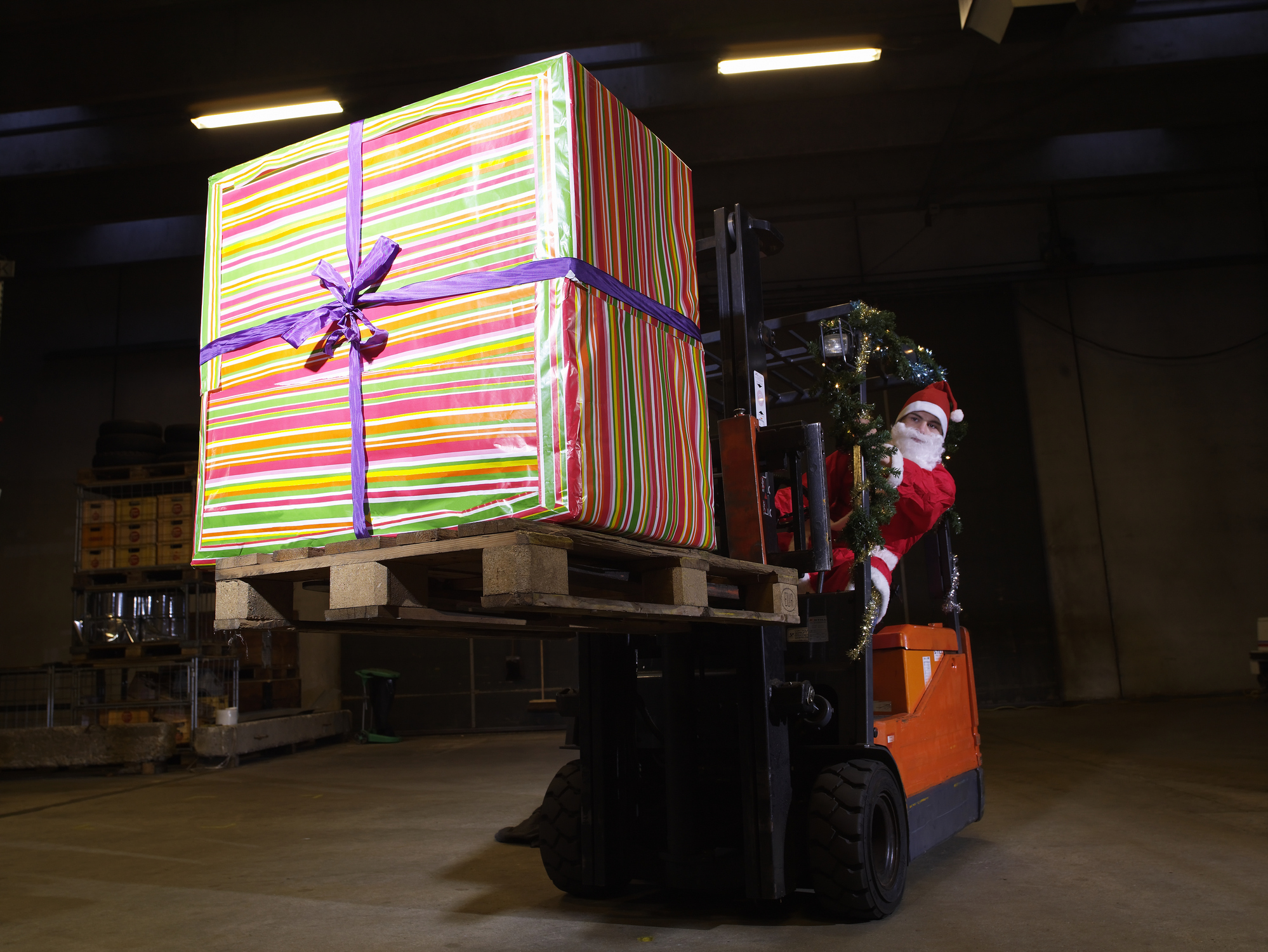 Santa driving forklift carrying big present in warehouse