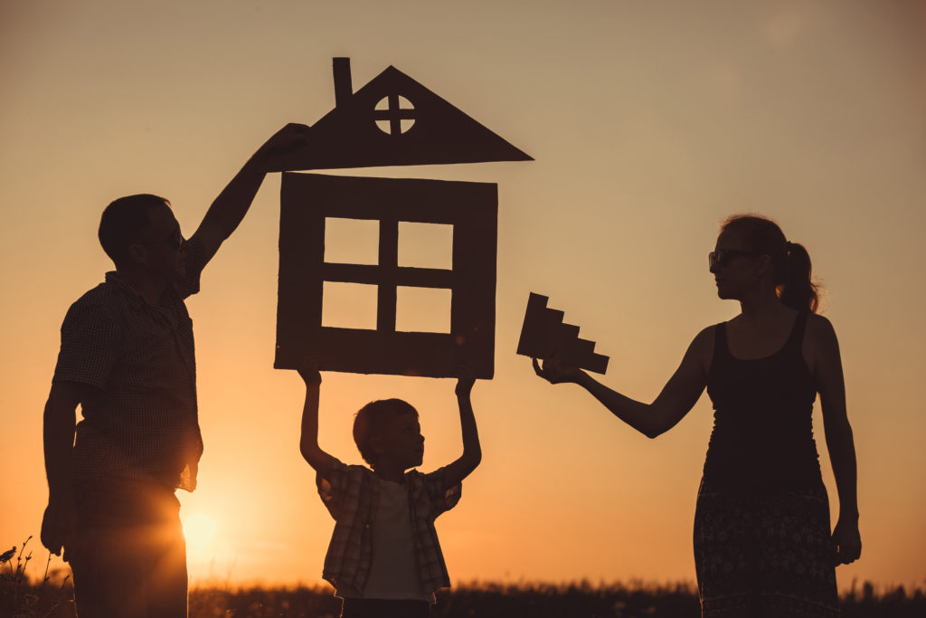 Happy family standing on the field at the sunset time. They build a house. Concept of friendly family.