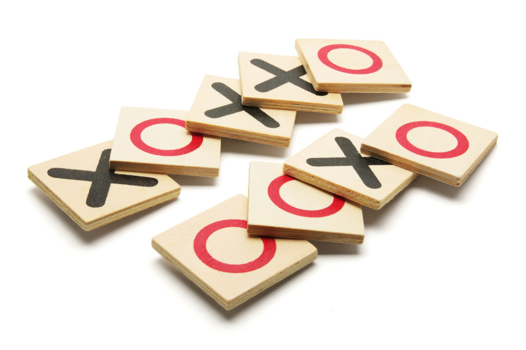 Tic-Tac-Toe Game on White Background with black Xs and red Os on light-colored wood blocks.