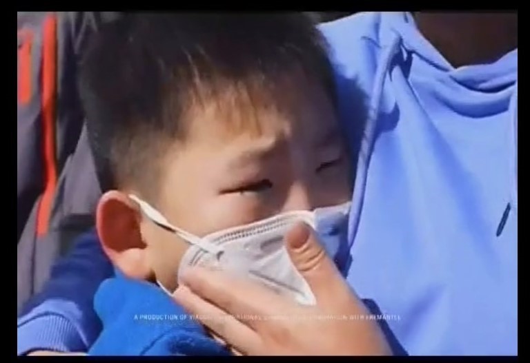 Asian child being hugged while wearing a face mask.