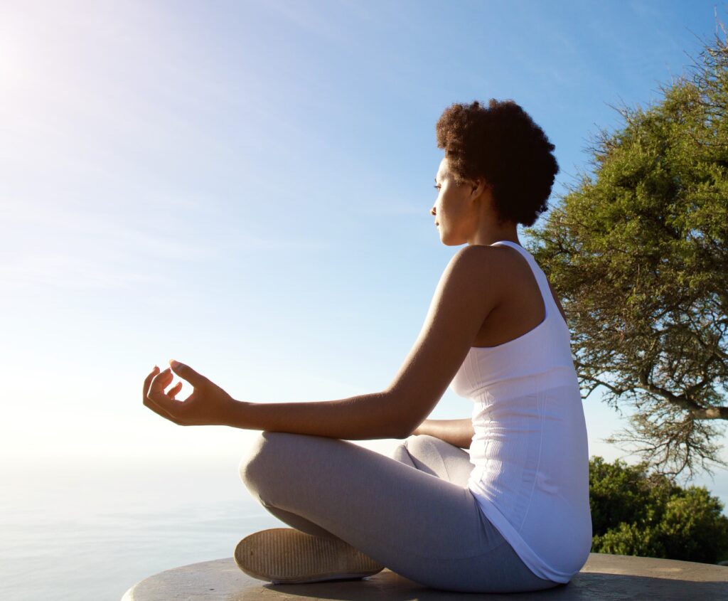 Side portrait of beautiful young woman sitting in yoga pose at beach