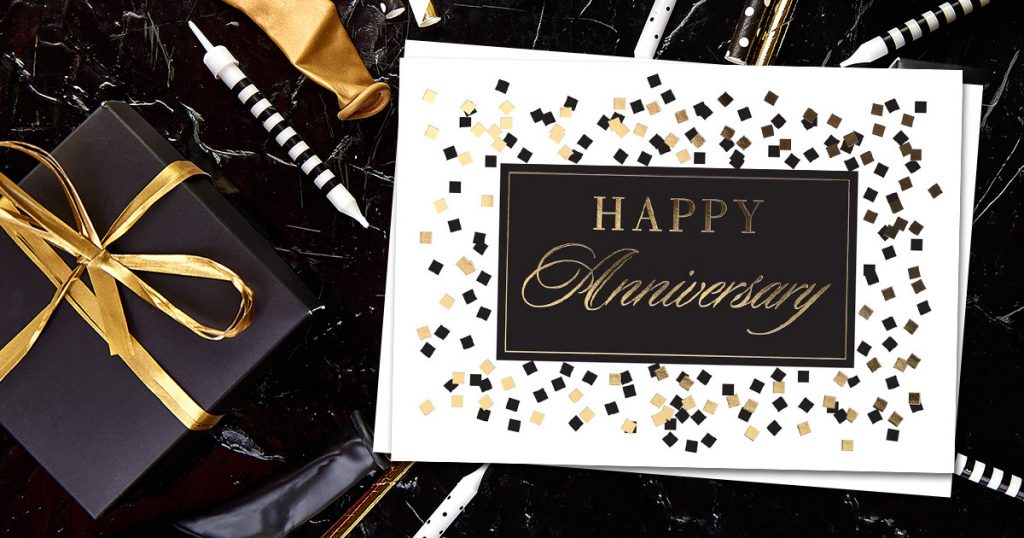 Elegant Anniversary card in black and gold from CardsDirect on a black and white marble background with black, white, and gold pens, a gold deflated balloon, and a black and gold gift.