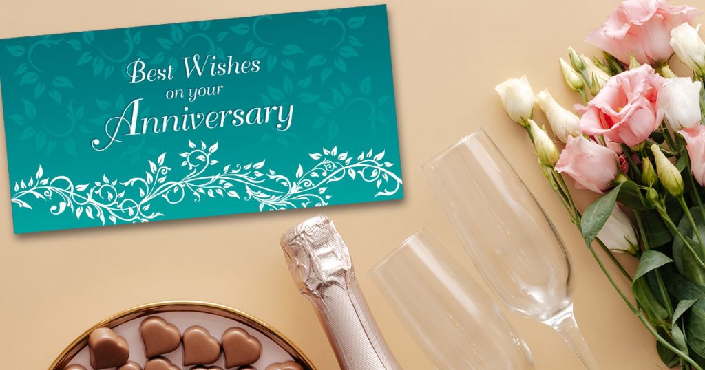 Stylish Tiffany blue and white wedding anniversary card from CardsDirect next to champagne, heart-shaped chocolates, and pink and white roses.
