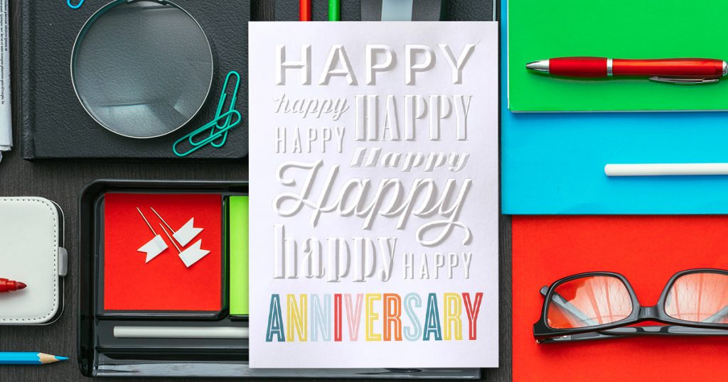 An embossed Anniversary card from CardsDirect on a background with colorful office supplies.