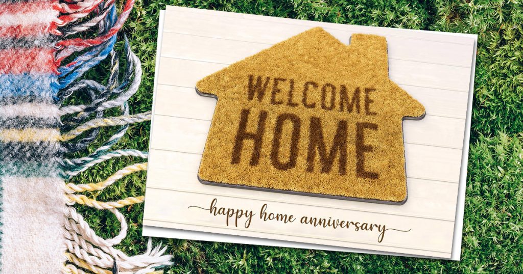 A CardsDirect New Home Anniversary card on a green grass background with a colorful blanket.