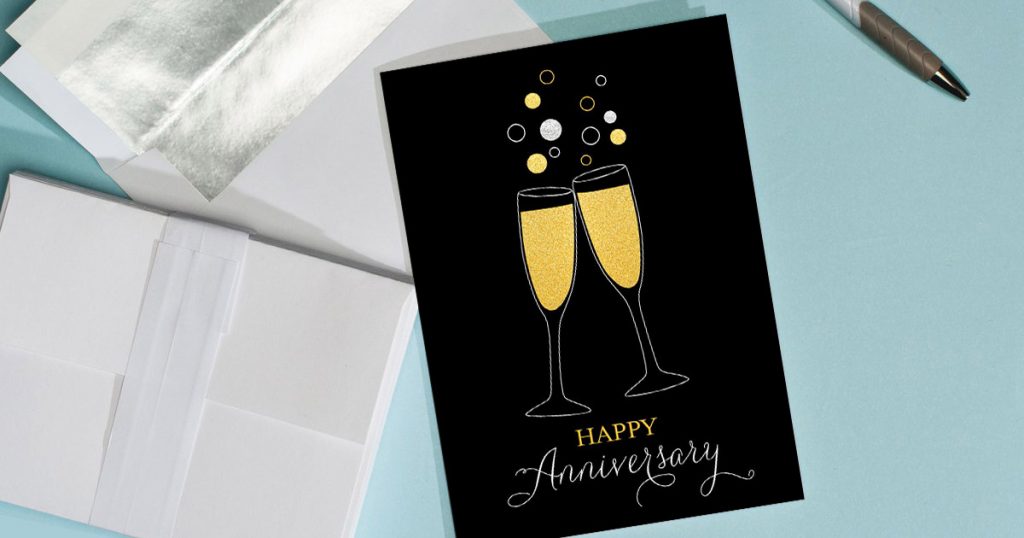 A Happy Anniversary card from CardsDirect with champagne glasses on it, placed next to a pen.