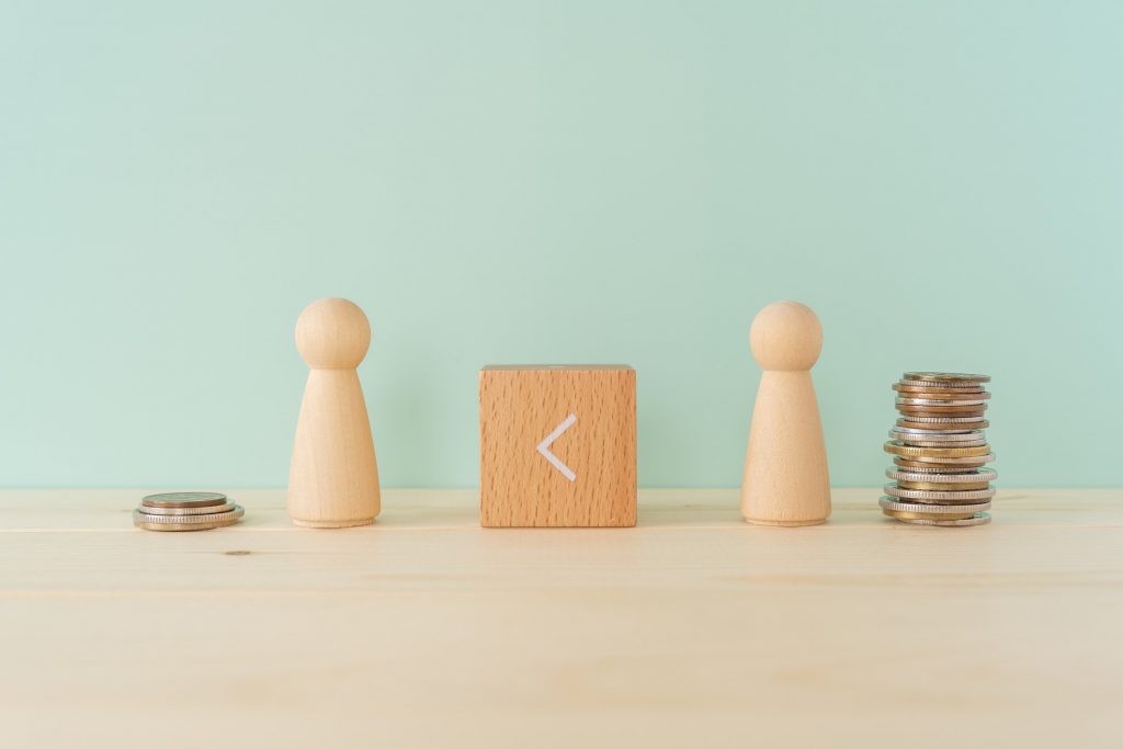 The gap between rich and poor; A wooden blocks with an inequality sign, many coins, and two human toys.