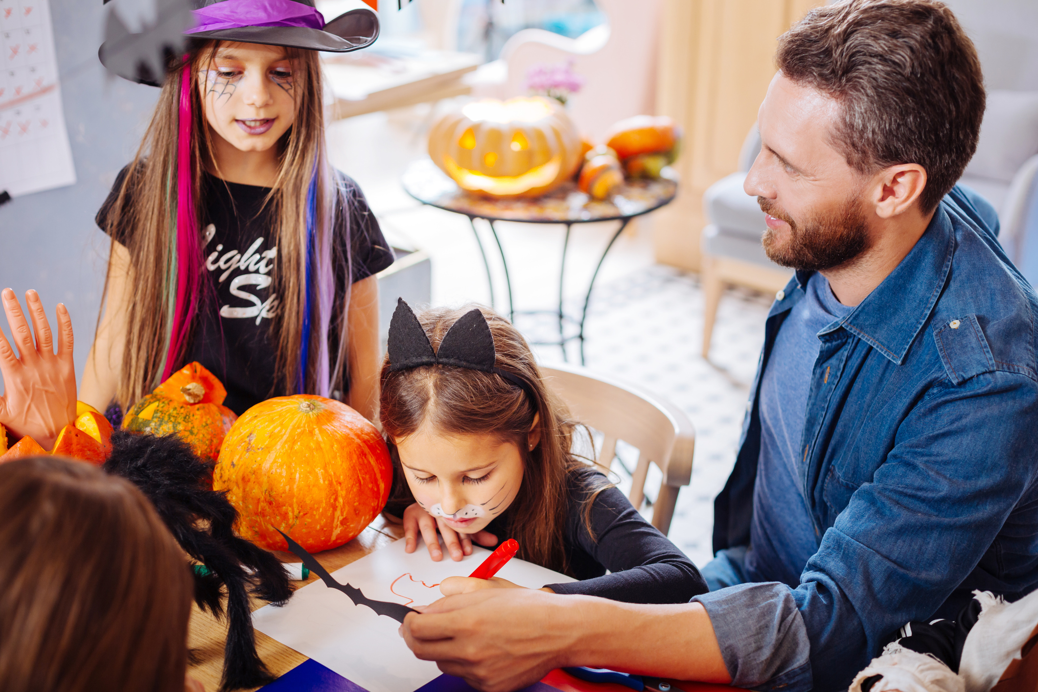 Father and daughters. Loving beaming handsome father helping his daughters coloring pictures for Halloween