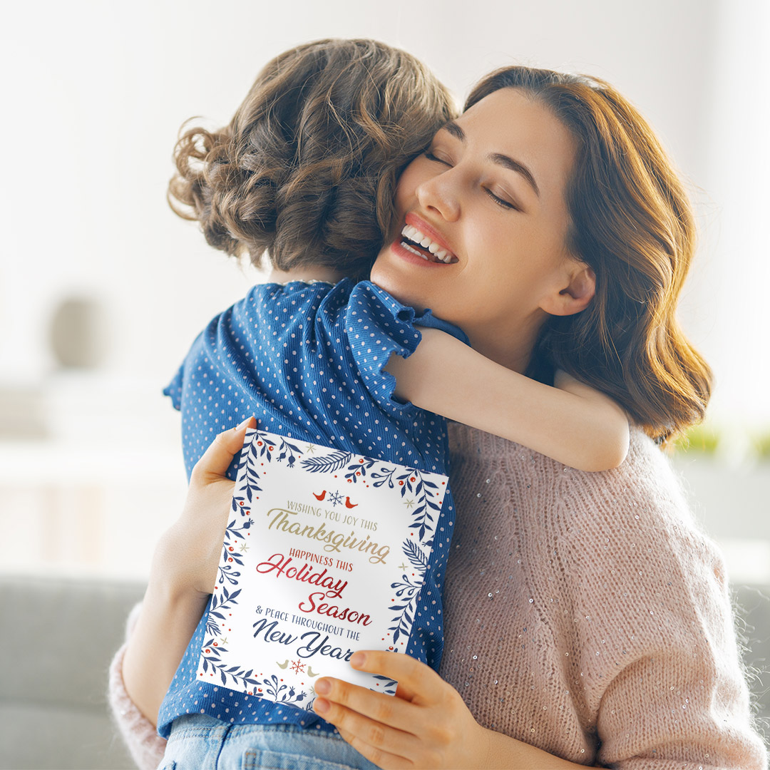 Small girl hugging mother who is holding a holiday card.