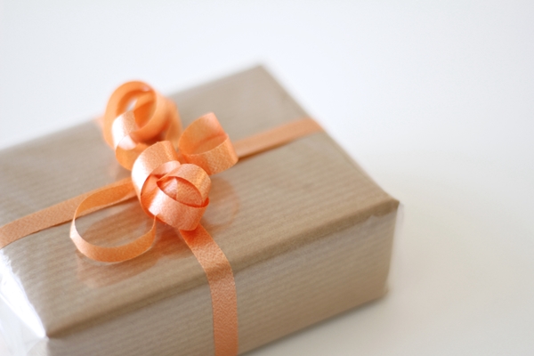A present with tan wrapping paper and orange curly ribbon.
